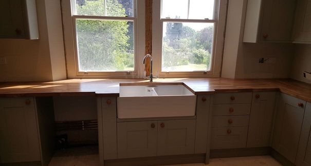 A new kitchen being installed with a belfast sink centered between uPVC windows