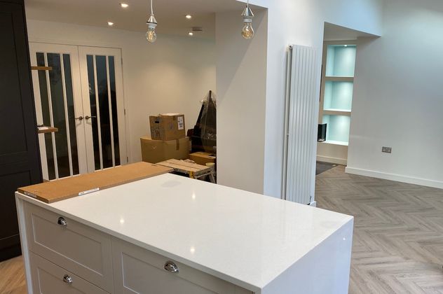 A modern kitchen with a white centered island set ontop of a herringbone kardean flooring